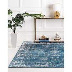 a blue area rug on a white floor next to a plant and bookshelf