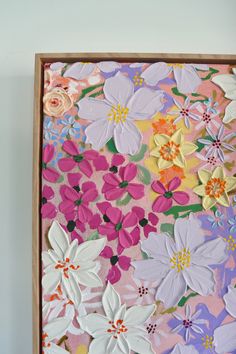 a painting with flowers painted on it in pink, yellow and purple colors is hanging on the wall