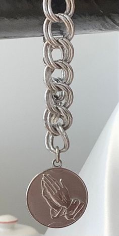 This beautiful Monet bracelet is a perfect addition to any jewelry collection. The sterling silver bracelet features a charming dangle charm with praying hands on the front and the serenity prayer on the back. The bracelet is 6 inches in length and has a double link chain type.  The bracelet is perfect for any occasion, whether it be a Christmas gift, anniversary gift, or birthday gift. It is also signed by the Monet brand, adding a touch of authenticity to the piece. The vintage style and relig Adjustable White Gold Charm Bracelet With Lobster Clasp, Silver Symbolic Bracelets With Dangling Charms, Symbolic Silver Bracelets With Dangling Charms, Symbolic Silver Bracelets With Charms, Symbolic Silver Bracelet With Dangling Charms, Silver Stainless Steel Charms With Lobster Clasp, Elegant Silver Chain Bracelet With Dangling Charms, Spiritual Silver Jewelry With Dangling Charms, Silver Hypoallergenic Charm Bracelet