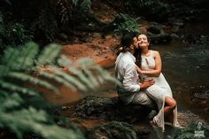 a man and woman are sitting on rocks in the water, hugging each other as they look at each other