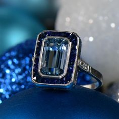 an emerald colored diamond ring sitting on top of a blue ornament