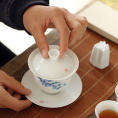 a person pouring tea into a cup on top of a wooden table next to cups and saucers