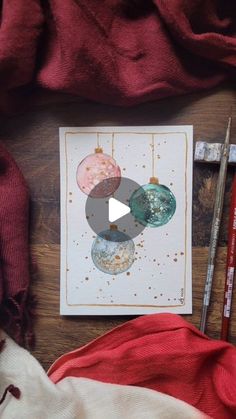 a card with ornaments on it sitting next to some paintbrushes and pencils