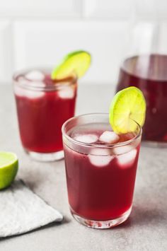 a glass filled with red liquid next to a bottle on top of a white counter