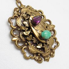 Large vintage rhinestone pendant is stunning in gold tone metal.   A green marbled glass stone and purple marquis rhinestone are prong set on the top of a stacked design.  Fleur de lis design is on the the side of the bottom layer.  On the second layter a vine of leaves surround it.  A unique beautiful vintage pendant.  I added a vintage Monet twisted serpentine chain so it is ready to wear.  Unmarked  beauty.  Pendant measures 1 7/8 X 1 5/8 inches and chain is about 23 1/2 inches long with a sp Jeweled Antique Gold Brass Jewelry, Vintage Oval Jeweled Necklaces, Vintage Jeweled Oval Necklace, Vintage Oval Jeweled Necklace, Green Vintage Charm Brass Jewelry, Green Brass Jewelry With Vintage Charm, Antique Green Jewelry With Vintage Charm, Bronze Gemstone Vintage Jewelry, Antique Jeweled Jewelry For Vintage Collection