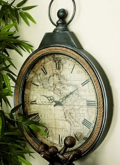 an old clock hanging on the wall next to a potted plant with green leaves