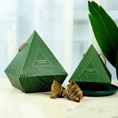 two green pyramids sitting next to each other on a white table with a plant in the background