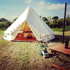 a tent set up in the middle of a field with two chairs and a table