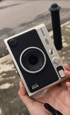 a person holding an old fashioned camera in their hand on the sidewalk near a street