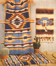 two rugs and a cactus in front of a wall hanging on a wooden frame