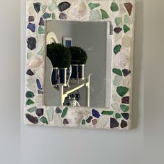 a mirror with sea shells on it and a plant in the middle is mounted to a wall