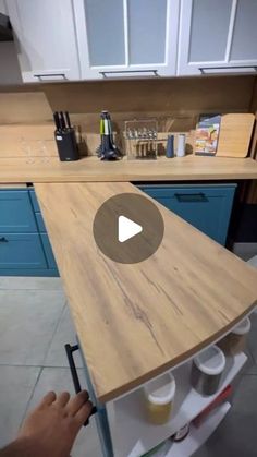 a person is painting the top of a wooden table in a kitchen with blue cabinets