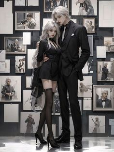 two people dressed in black standing next to each other with pictures on the wall behind them