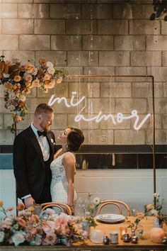 a bride and groom standing next to each other in front of a table with flowers