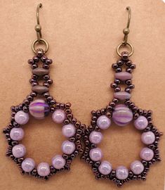 Fatima Earrings in plum have a wreath of round purple beads and larger melon bead. Edges are dark wine seed beads, Stem is made from dusky purple SuperDuo beads and seed beads. They dangle from antique brass jump ring and ball end ear wire. Design by Denise Berryhill of DBBeadingDesigns on Etsy. Created by TLP of Takeen Arts. Item E631. Purple Dangle Beaded Earrings With Spacer Beads, Purple Dangle Earrings With Tiny Beads, Purple Beaded Dangle Earrings With Tiny Beads, Pink Beaded Earrings With Bead Caps, Handmade Round Czech Glass Beaded Earrings, Czech Glass Beaded Earrings With Spacer Beads, Purple Czech Glass Beads For Jewelry Making, Purple Beaded Earrings With Dangling Round Beads, Purple Beaded Oval Jewelry