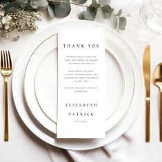 a place setting with white plates and gold cutlery, silverware and greenery