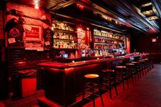 a dimly lit bar with stools and red lights on the walls, along with several shelves