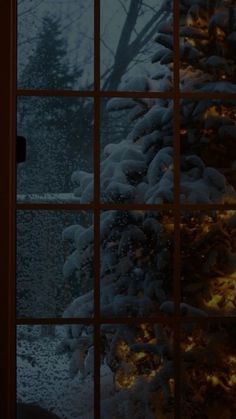 a window with snow on the outside and lights in the inside, looking out onto a snowy forest