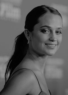 a black and white photo of a woman with long hair smiling at the camera,