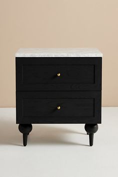 a black and white nightstand with two drawers on it's legs, against a beige wall