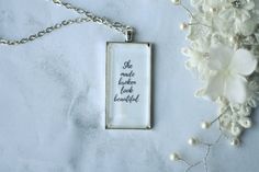 a necklace with the words she made another look beautiful on it next to some flowers