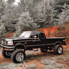 a black pickup truck parked on top of a dirt road in front of some trees