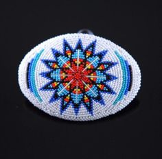 a white and blue beaded brooch with an orange, yellow, and red design on it