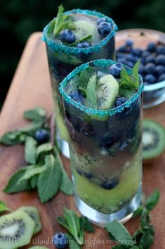 two glasses filled with blueberries and kiwis on top of a wooden table