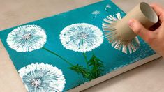 a person is using a paper mache to paint dandelions on a canvas