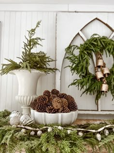 pine cones are in a white bowl on a mantle with evergreen branches and other holiday decorations