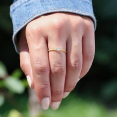 a woman's hand with a diamond ring on top of her finger, in front of some bushes