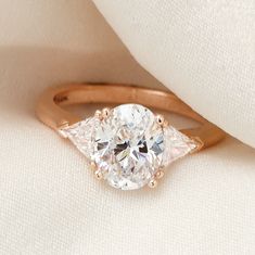 an oval diamond ring with two pear shaped diamonds on the band, set in 18k rose gold