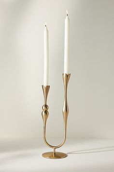 two white candles sitting on top of a gold candle holder in the shape of a twig