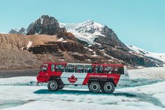 a red and white tour bus on ice with mountains in the background