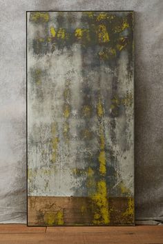 an abstract painting with yellow and grey colors on a wooden floor next to a gray wall