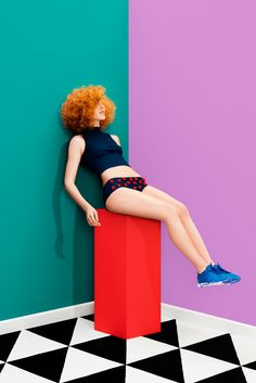 a woman laying on top of a red box in front of a purple and blue wall