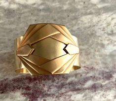 Wonder Woman 1984 wants you to save the world in this wide brass Gatsby era cuff with a geometric art deco design.

 	The smooth scrubbed brass cuff is 1 1/2" wide (approximately 4cm).
 	6" (15cm) from end to end.
 	Weight: 1.4 oz.
 	This is a handmade cuff made from new findings.
 	Read the FAQ to learn more about the care and safe-keeping of natural unfinished brass.

Yes! Custom sizing is available. Cuff can be made smaller or larger while shaping. Contact us to make a custom request. See the Wonder Woman 1984, Art Deco Bracelet, Brass Cuff, Wide Bracelet, Gold Art Deco, Save The World, Bracelet Cuff, Gold Art, Art Deco Design