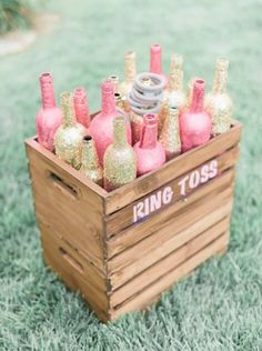 a wooden crate filled with lots of pink and gold wine bottles on top of green grass