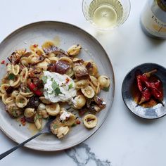 a plate of pasta with meat and vegetables next to a bottle of wine