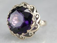 "A gorgeous purple amethyst with flashes of indigo and plenty of glitter is the centerpiece of this fabulous mid-century cocktail ring. A pierced scrolling scallop frame adds graphic interest and makes this piece unique to other ornate cocktail rings! Metal: 14K Yellow Gold Gem: Amethyst 17.69 Carats Gem Measurements: 17.2 mm, Round Ring Size: 6 Marks: \"14K\" Stamped on the inside band SKU #: N7UDRCEV Each piece has been identified and graded by a Graduate Gemologist who has been certified by t Yellow Gold Sapphire Ring, Amethyst Cocktail Ring, Right Hand Ring, Vintage Cocktail Ring, Cameo Ring, Right Hand Rings, Hand Ring, Round Rings, Anniversary Ring