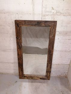 a wooden mirror hanging on the wall in a room with white walls and concrete flooring