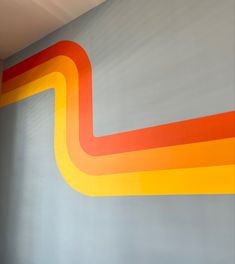 an orange and yellow painting on the side of a gray wall next to a window