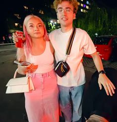 a man and woman standing next to each other in front of a red car at night