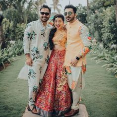 three people standing next to each other in front of some trees and grass with palm trees behind them