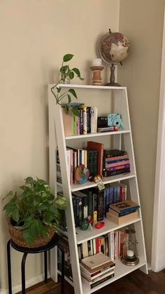 a tall white book shelf with books on top and plants in the corner next to it