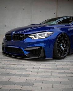 a blue bmw car parked in front of a building with its hood up and lights on