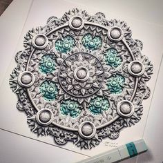 a drawing of an intricate design on white paper with blue and green markers next to it