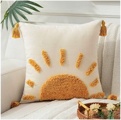 a decorative pillow with yellow tassels on it sitting next to a basket and potted plant