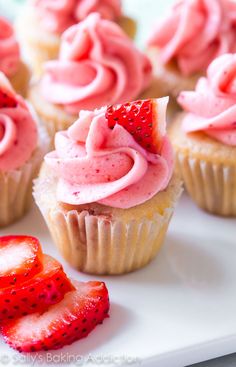 cupcakes with pink frosting and strawberries on a white plate next to some sliced strawberries