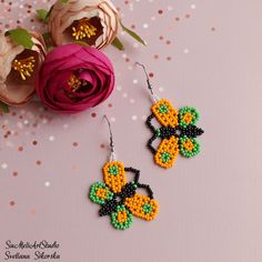 a pair of beaded earrings sitting on top of a table next to pink flowers